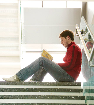 Male student reading book on stairs.