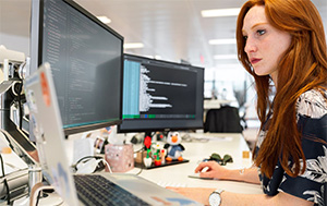 Woman in office using a computer with two screens.